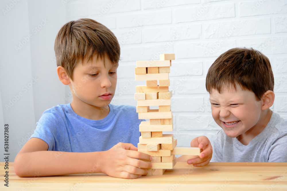 Wall mural children play the board game jenga, boys build a tower of wooden cubes, the concept of fine motor sk