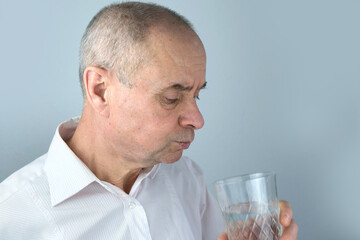 close-up of mature charismatic man, senior 60 years drinks clean water from glass, takes pill,...