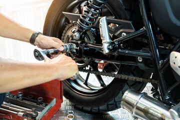 Mechanic using a wrench and socket to Remove and Replace Rear Motorcycle Wheel, working in garage maintenance, repair motorcycle concept  .selective focus