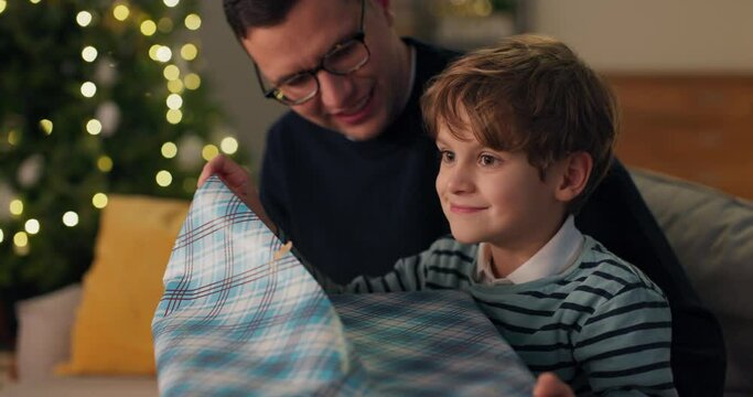 A young boy opens a gift from Santa Claus, enjoys the gift tears the colored paper, a large box with a dream toy.