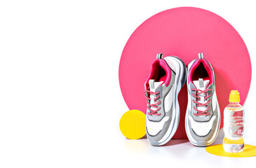 Bright lit scene with chunky sneakers, bottle of water against the pink and yellow background. Reducing weight, getting fit and healthy lifestyle. Casual footwear. Minimalist fashion fitness concept.