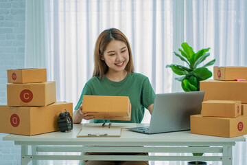 young asian woman successful online sales at home by sending parcels working with laptop to take...