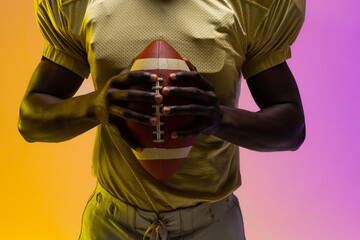 Midsection of african american male american football player with neon purple and yellow lighting © wavebreak3