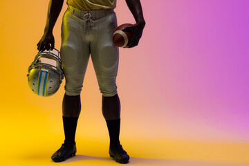 Midsection of african american male american football player with neon purple and yellow lighting