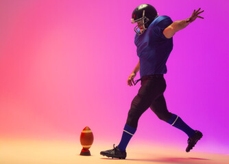 Fototapeta na wymiar Caucasian male american football player kicking ball with neon pink lighting