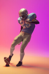 Obraz na płótnie Canvas African american male american football player kicking ball with neon pink lighting
