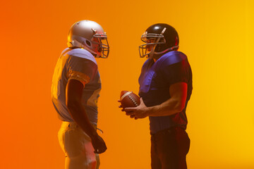 Fototapeta na wymiar Diverse male american football players holding ball with neon orange lighting