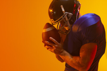 Caucasian male american football player holding ball with neon orange lighting © wavebreak3