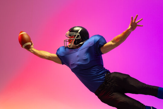 Caucasian male american football player holding ball with neon pink lighting - Powered by Adobe