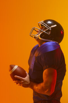 Caucasian male american football player holding ball with neon orange lighting
