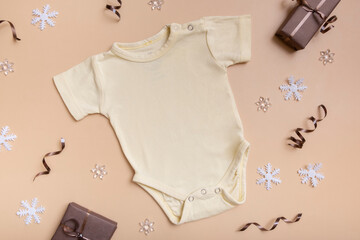 Yellow baby bodysuit mockup for logo, text or design on beige background with winter decotations top view