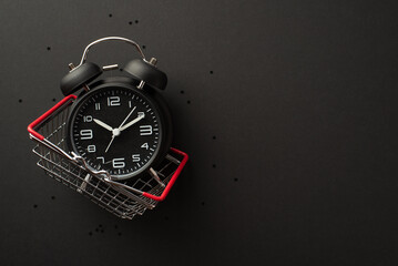 Black friday concept. Top view photo of black alarm clock in shopping cart and confetti on isolated...