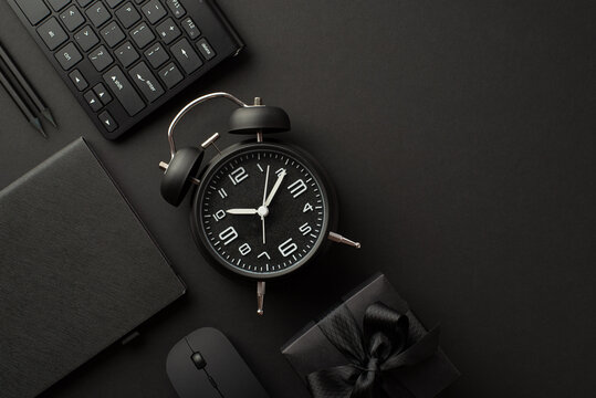Black friday concept. Top view photo of black gift box with ribbon bow alarm clock planner pencils computer mouse and keyboard on isolated black background with copyspace