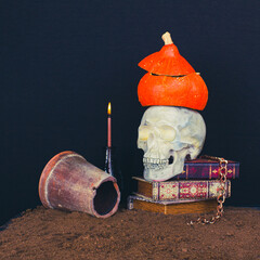 Halloween still life with a vintage skull, books, necklace, pumpkin  and candle on a dark background with copy space.