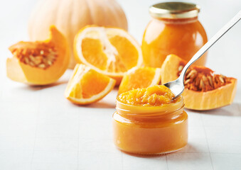 Spoon of tasty pumpkin jam on jar, slices of orange and pumpkin on light background. Conserve...
