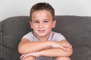 Portrait of a Funny little boy smiling and laughing looking at camera sitting on the couch at home. Concept of a happy childhood. High quality photography