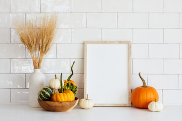 Autumn still life. Photo frame template, decorative pumpkins, vase of dry wheat on white table....