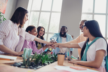 Photo of friendly cute businesspeople making arms stack teambuilding indoors workstation workshop...