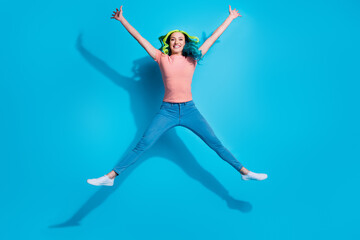 Fototapeta na wymiar Full length size image of cheerful young girl jumping up in star pose fooling around isolated on blue color background