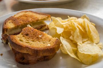Grilled cheese with ham sandwich on plate with potato chips in a diner.

