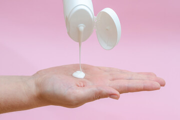 Woman's hand squeezing body lotion isolated on pink background. Beauty concept. Tube for cosmetic products