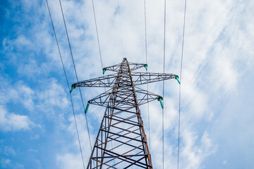 High voltage, power transmission line on the mountain range on a blue sky background. Overhead power line in the mountains. Metal poles of power lines in the mountains