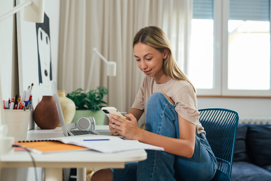female college student remote work from her home. using mobile phone and sitting desk in her room
