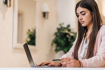 Serious young adult woman, entering her credit card number in laptop.