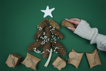 A woman's hand lays out a Christmas tree made of pine cones