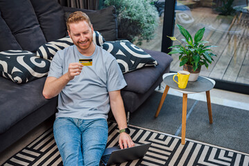 Cheerful young adult man, putting in his credit card info in his laptop, at home.