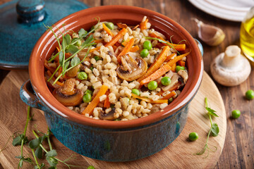 Pearl barley grain porridge with carrot, mushrooms, green peas and onion. Lenten vegetarian dish.