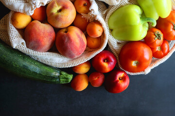 Reusable mesh bags for fruits and vegetables, filled with various healthy food. Dark background, top view.