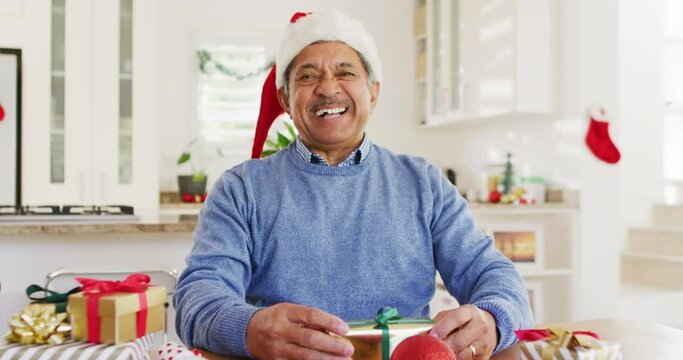 Video of happy senior biracial man in santa hat making christmas video call, smiling to camera