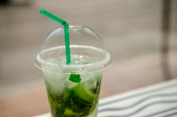A glass of non-alcoholic mojito cocktail, in a plastic glass with a plastic tube, in the sun in a cafe on the background of the city