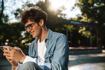 Portrait of young handsome smiling boy in glasses watching phone