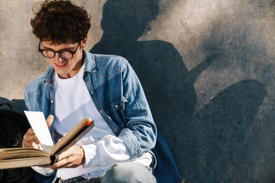 Portrait of young curly smiling boy in glasses reading book