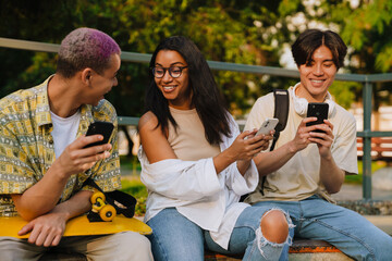 Three young smiling happy friends with phones sitting together