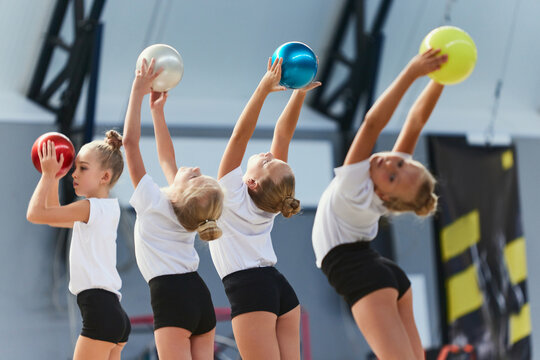 Little girls, beginner gymnastics athletes doing exercises with gymnastics equipment at sports gym, indoors. Concept of studying, achievements, skills
