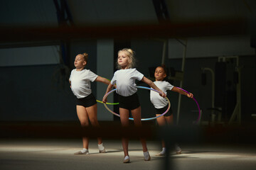 Flexible little girls, female rhythmic gymnasts training with gymnastic hoop at sport gym, indoors....