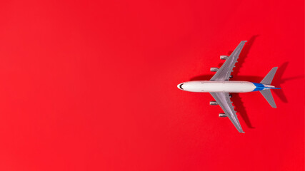 Top view of white model plane, airplane toy on isolated red background. Flat lay with copy space. Trip or travel banner..