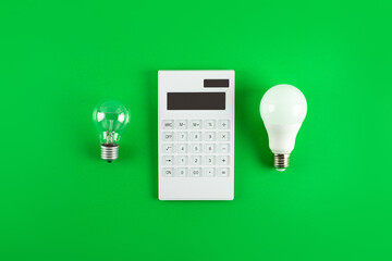 White calculator and incandescent lamp or LED bulb on green background. Concept showing the payment...