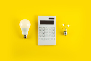 White calculator and incandescent lamp or LED bulb on yellow background. Concept showing the payment of electricity bills. The concept of savings electricity. Reducing the payment of utility bills..