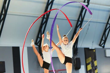 Two little girls, female rhythmic gymnast training with multicolored ribbons at sport gym, indoors....