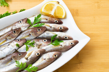 Fresh uncooked haddock fishes on in ceramic dish on table, raw whiting fish concept