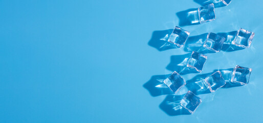 Top above overhead close up macro view photo of ice cubes and water drops on blue background with copy empty blank space.