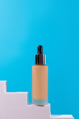 Cosmetic liquid foundation nude cream bottle mockup on white podium pedestal. Beige concealer base cosmetics product mock up on blue background. Skincare beauty primer, bb cc corrector.