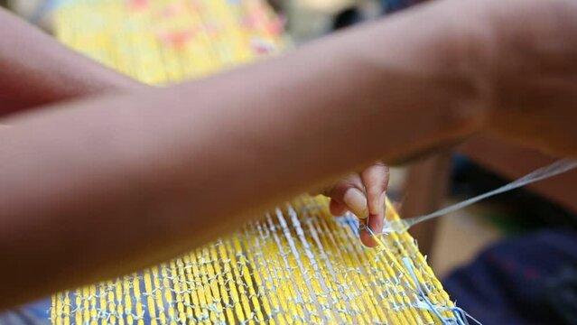 Closeup hands of old female person making Mudmee cloth, a handicraft for woman at home in rural Thailand 