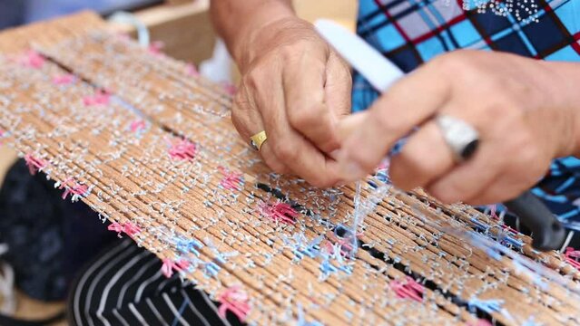 Closeup hands of old female person making Mudmee cloth, a handicraft for woman at home in rural Thailand