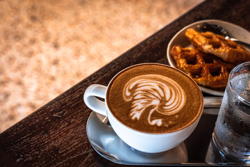 Hot coffee latte with latte art milk foam in a swan shape in cup mug and Homemade Belgian Waffles with honey on wood desk on top view. As breakfast In a coffee shop at the cafe,during business work.