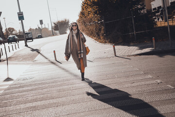 Photo of positive shiny lady dressed warm coat dark eyewear purse enjoying fall sunny weather crossing street outdoors urban town road